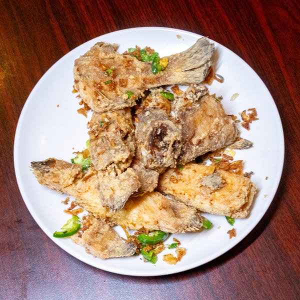 Crispy fried fish pieces with green peppers and fried garlic on a white plate.