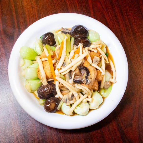 A white plate of stir-fried bok choy, mushrooms, carrots, and tofu in a savory sauce.