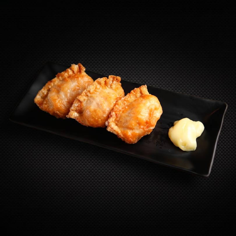 Three golden-brown fried dumplings with a dollop of mayonnaise on a black rectangular plate.