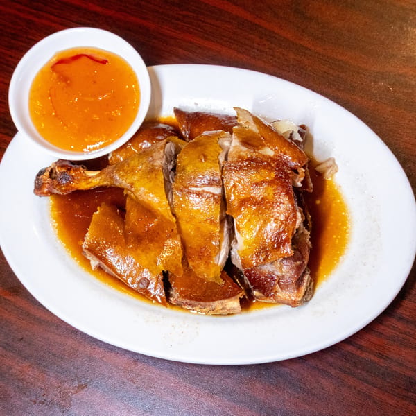 Roasted duck, cut into pieces and covered in sauce, served with a side of orange dipping sauce.
