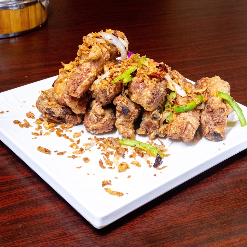 Crispy fried pork ribs with onions, green peppers, and fried garlic on a white plate.