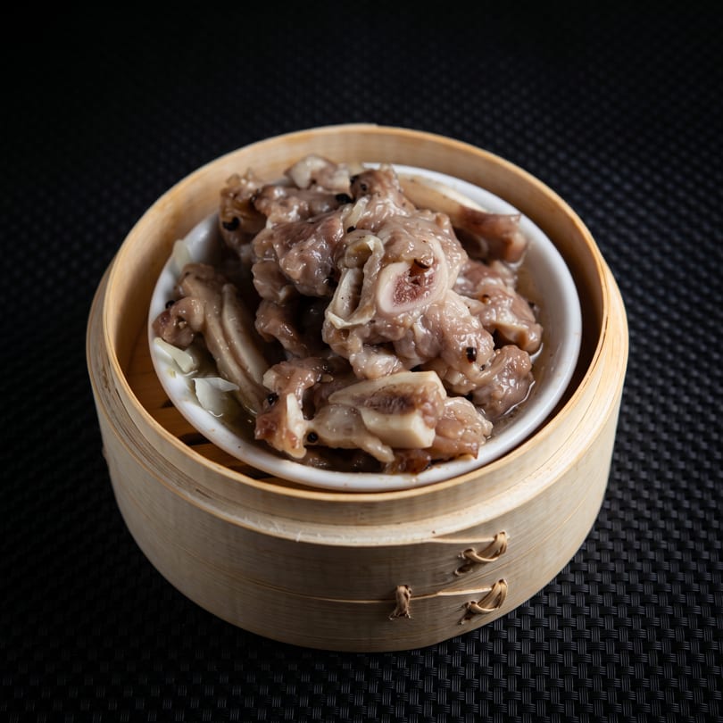 Steamed pork ribs with black beans in a white dish, served in a bamboo steamer.