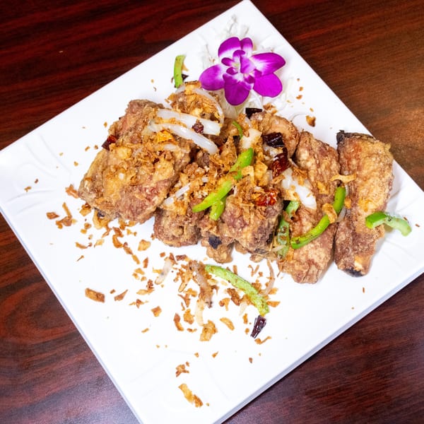 Crispy fried chicken wings topped with fried garlic, onions, green peppers, and a purple orchid.