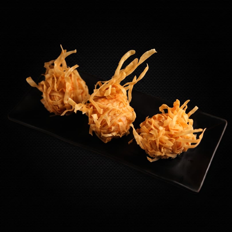 Three crispy, golden-brown fried wonton balls on a black rectangular plate against a dark background.