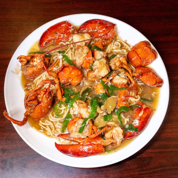 A white plate filled with lobster meat, noodles, green peppers, and mushrooms in a savory sauce.