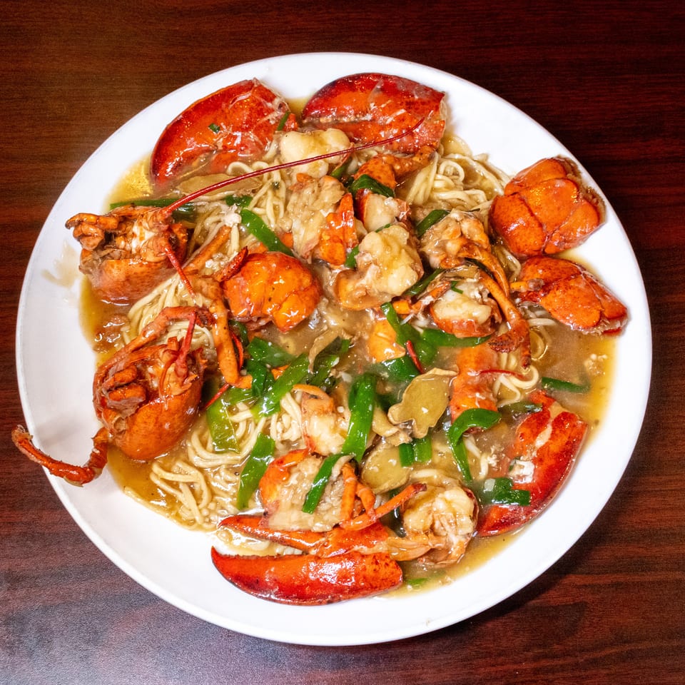 A white plate filled with lobster meat, noodles, green peppers, and mushrooms in a savory sauce.